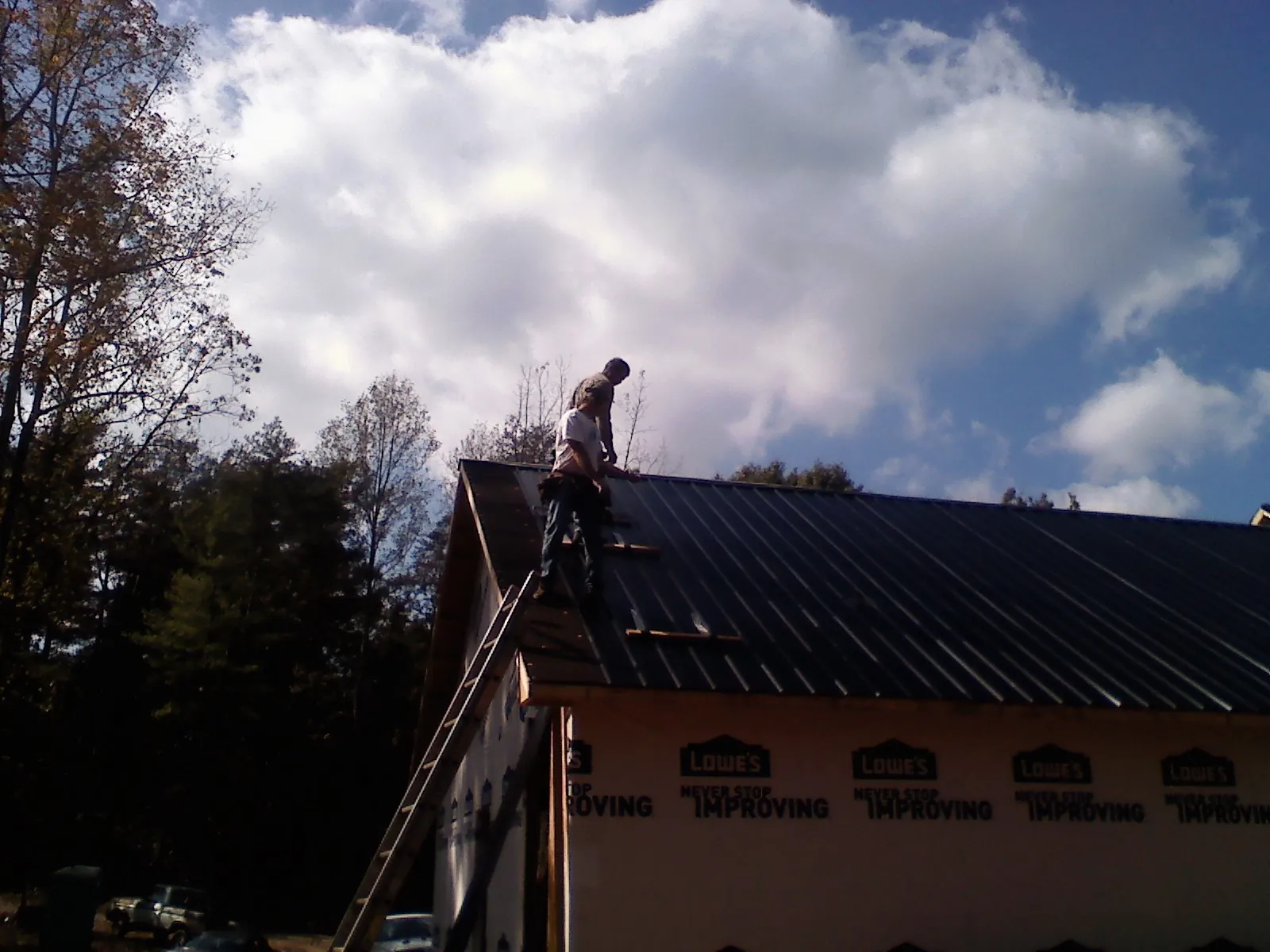 Roofer fastening dark metal panels high against a cloudy sky, from a Roof Inspection job in Bunker Hill